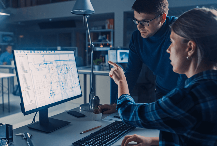 woman pointing at computer screen with man standing to her side